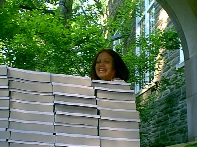 Jackie Vega, returning for her second year, smiles from behind a pile of general education books and undergraduate degree program bulletins. 