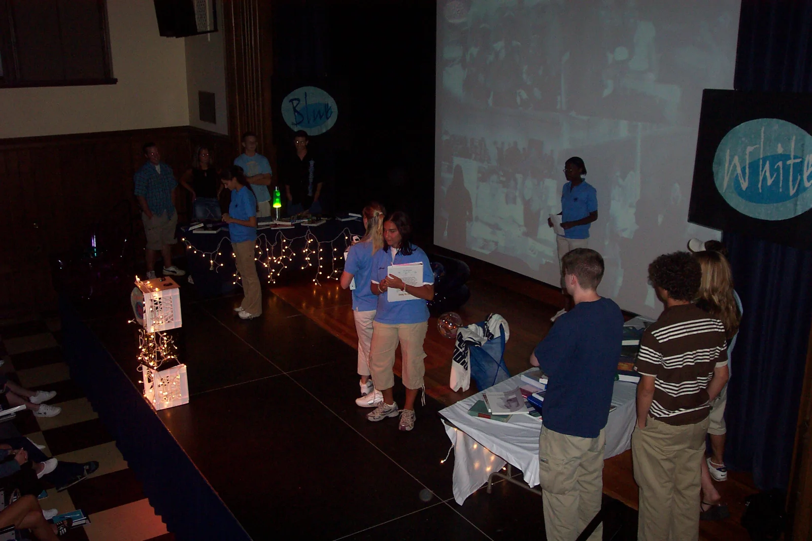 The contesants watch politely as the orientation leaders talk about the advantages of becoming involved.