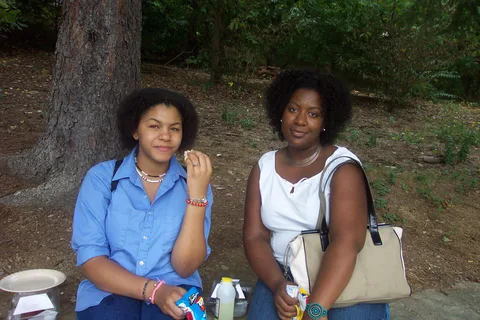 New student Danielle Taylor chats with a friend in the shade of evergreen trees. 