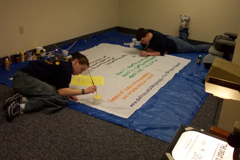 Later, the banner is taken off the wall and is painted with acrylic paints based on the colors from the original transparency.