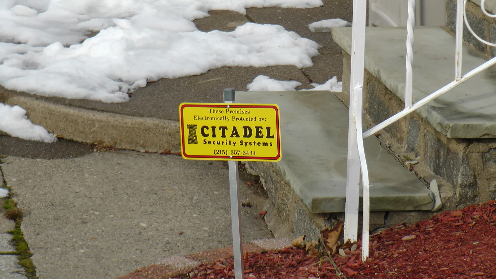 A sign reminding passers-by that the house is monitored remotely through the installed security system.
